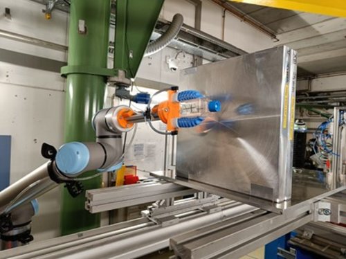 Figure: a cell culture flask is held in the radiation field of the GCR simulator by the robotic arm behind the shielding material.