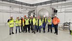 Eine Gruppe Menschen steht vor der Vakuumkammer im Inneren eines Betongebäudes.