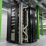 KI-System mit Direct Liquid Cooling im GSI-Höchstleistungsrechenzentrum Green IT Cube In einem industriellen Raum mit grünen Metallsäulen steht ein schwarzer Server mit silbernen Verrohrungen.