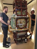 Zwei Männer stehen rechts und links von einem überkopfhohen, verschachtelten Holzgerüst.