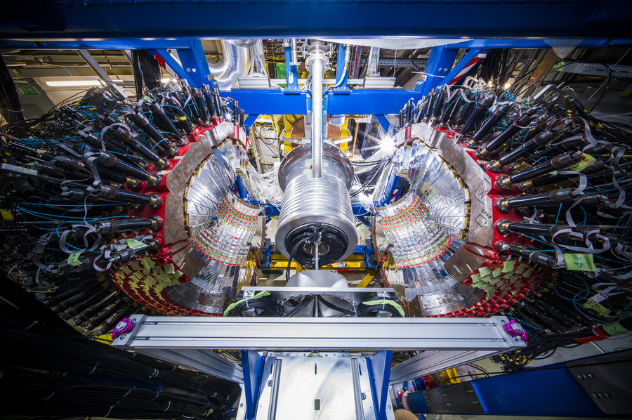 The experimental setup in maintenance position Zwei silbern glitzernde Halbkugeln stehen zu den Seiten eines silbernen Zylinders. Viele Kabel führen an den Seiten weg.
