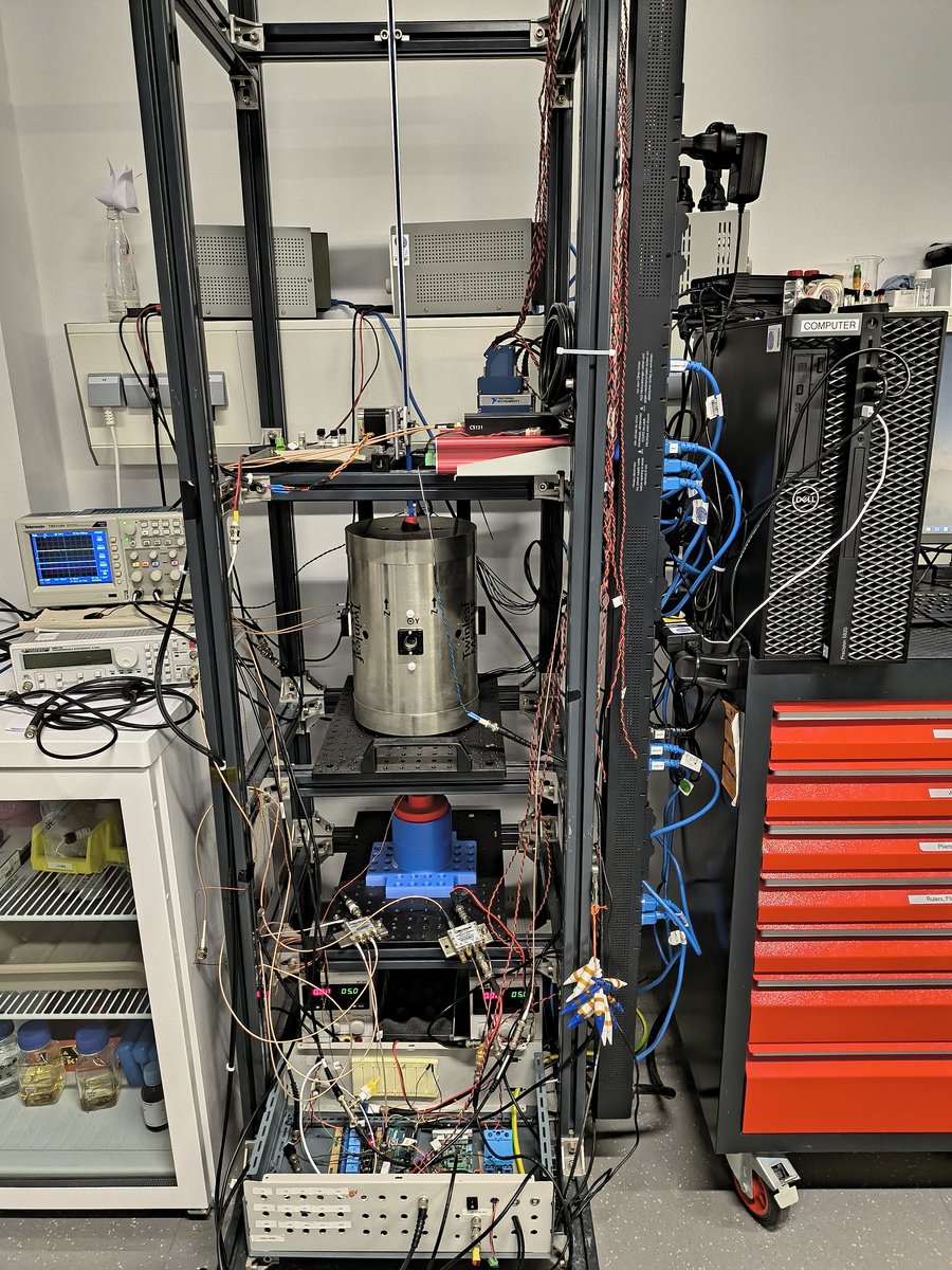 In einem Metallregal steht ein silberner Zylinder, darunter und darüber Messgeräte und Kabel.