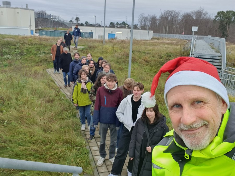 Visit of the participants at the FAIR viewpoint Eine Reihe Menschen steht in einer Schlange im Grünen. Ganz vorne steht ein Mann mit Nikolausmütze.