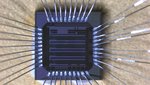 Microchip with a side-length of 1,5 millimeters, equipped with circuits for particle detector readout. Von einem grauen, rechteckigen Mikrochip gehen in alle Richtungen dünne Drähte weg.
