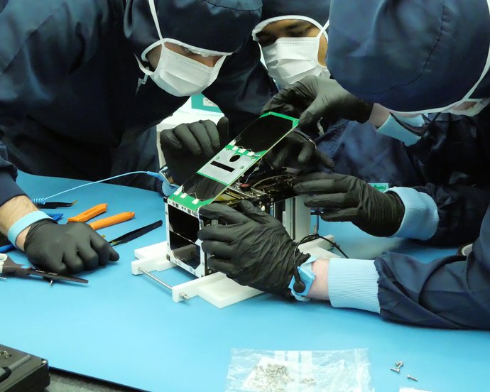 Mehrere Personen in Schutzanzügen beugen sich über einen rechteckigen Kasten mit Elektronik.