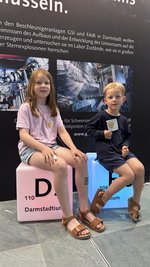 Children sitting on two glowing cubes representing the elements Darmstadtium and Hassium, discovered at GSI.
