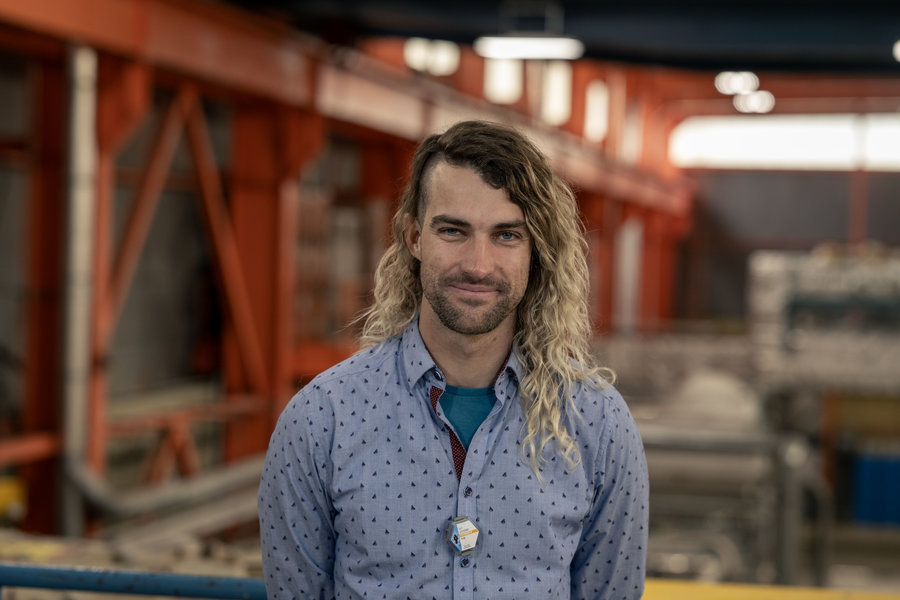 Dr. Guy Leckenby Ein Mann mit halblangen braun-blonden Haaren und einem blauen Hemd steht in einer Halle.